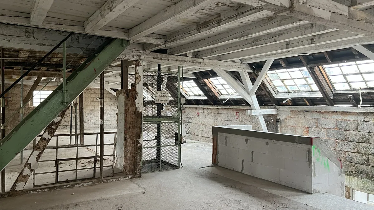 Denkmalgeschützte Fabrikhalle im Bestand mit Sandsteinwänden, Stahlstützen und Sheddach